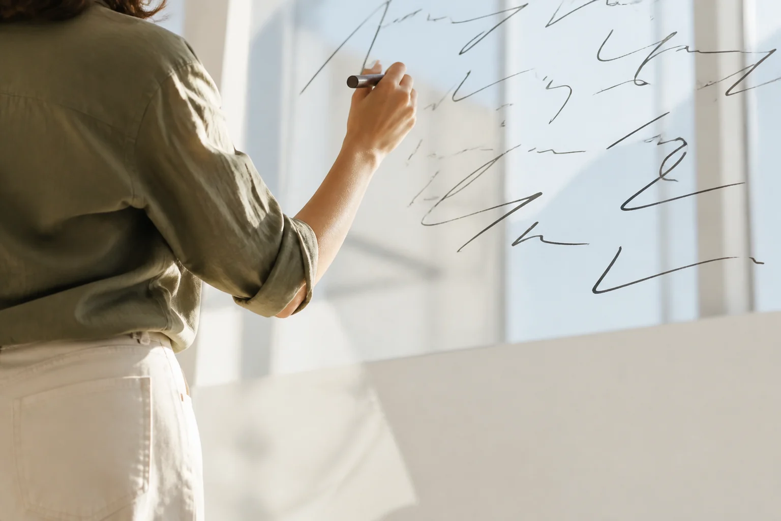 Person drawing expressive lines on a sunlit glass wall